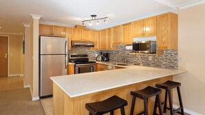 A modern kitchen with wooden cabinets, a large island with bar stools, stainless steel appliances, and a tiled backsplash.