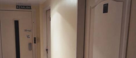 Un pasillo con un letrero que indica la salida, una puerta con manija y una lámpara en el techo.