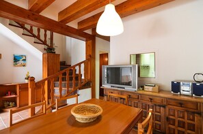 Una mesa de comedor de madera con una cesta tejida, un televisor y altavoces sobre un mueble de madera.