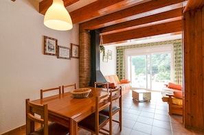 Un comedor con una mesa y sillas de madera, una lámpara colgante y vistas al exterior a través de un ventanal.