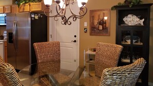 Une cuisine avec des chaises en osier, un lustre et un meuble vitrine pour les bouteilles de vin.