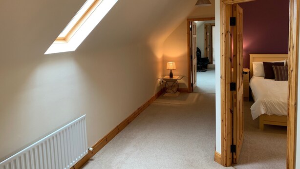 A bedroom with a skylight, a bedside table with a lamp, and a bed with pillows. - Racecourse Lodge Apartment (Clifden)