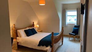 A bedroom with a bed, bedside tables, a lamp, a chair, and a window. - Racecourse Lodge Apartment (Clifden)