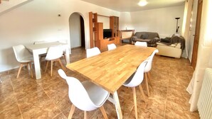 Un'ampia zona giorno con un tavolo da pranzo in legno, sedie bianche, un divano e una televisione.