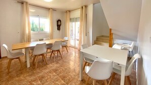 Un'ampia sala da pranzo con un tavolo in legno e sedie bianche, una sveglia appesa al muro e una scala che conduce a un piano superiore.