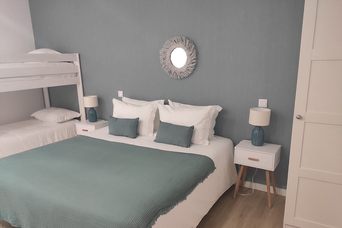 Quarto com uma cama beliche, uma cama de solteiro e uma mesa de cabeceira com luminária.