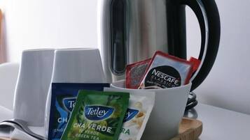 A tray with a kettle, two cups, and packets of tea and coffee.