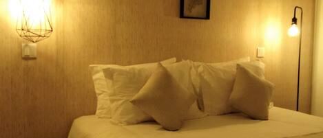 A bed with white linens and pillows, a small round wicker side table, and two wall-mounted light fixtures.