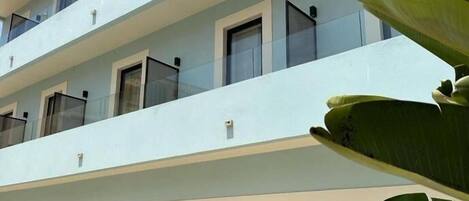 A multi-story hotel with a light blue facade, balconies, and potted plants.