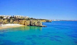 Un hôtel situé sur la côte, avec une plage de sable, une eau cristalline et des falaises rocheuses.