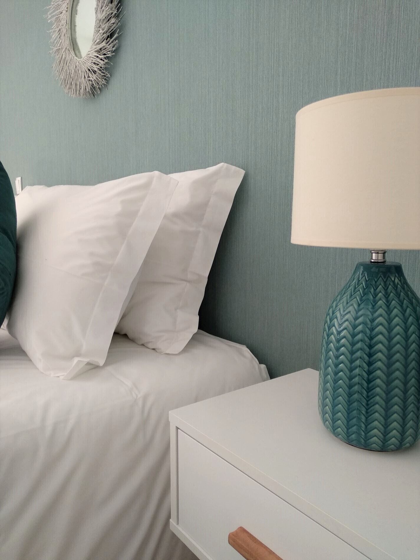 A bedroom with a bed, pillows, a nightstand, a lamp, and a wall mirror.
