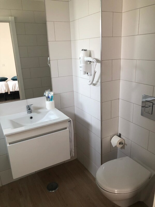 A bathroom with a white sink, toilet, and a hairdryer mounted on the wall.
