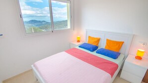 A bedroom with a bed, two bedside tables, a window, and a view of the outdoors.