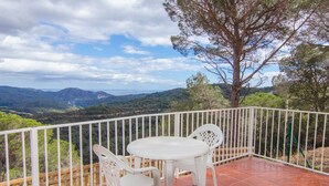A balcony with white plastic chairs and a table, overlooking a mountainous landscape.