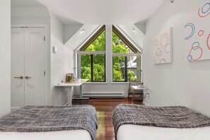 Ein Schlafzimmer mit zwei Betten, einem Schreibtisch und einem großen Fenster.
