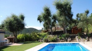 A rectangular swimming pool with a clear blue water surface, surrounded by a well-maintained lawn and various trees. - Club Villamar - Lovely villa for 6 persons with private swimming pool and big garden (Calonge)