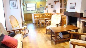 A cozy living room with a fireplace, wooden furniture, and a kitchen in the background. - Club Villamar - Lovely villa for 6 persons with private swimming pool and big garden (Calonge)