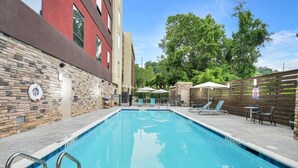 A rectangular swimming pool with a stone wall on one side and a wooden fence on the other.