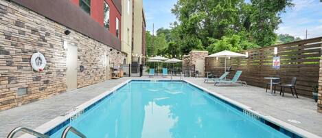 A rectangular swimming pool with a stone wall on one side and a wooden fence on the other.