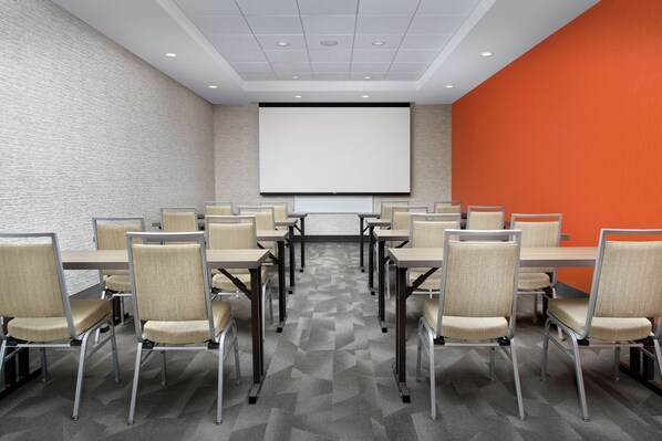 Una sala de conferencias con una pantalla grande, varias mesas y sillas dispuestas para reuniones.