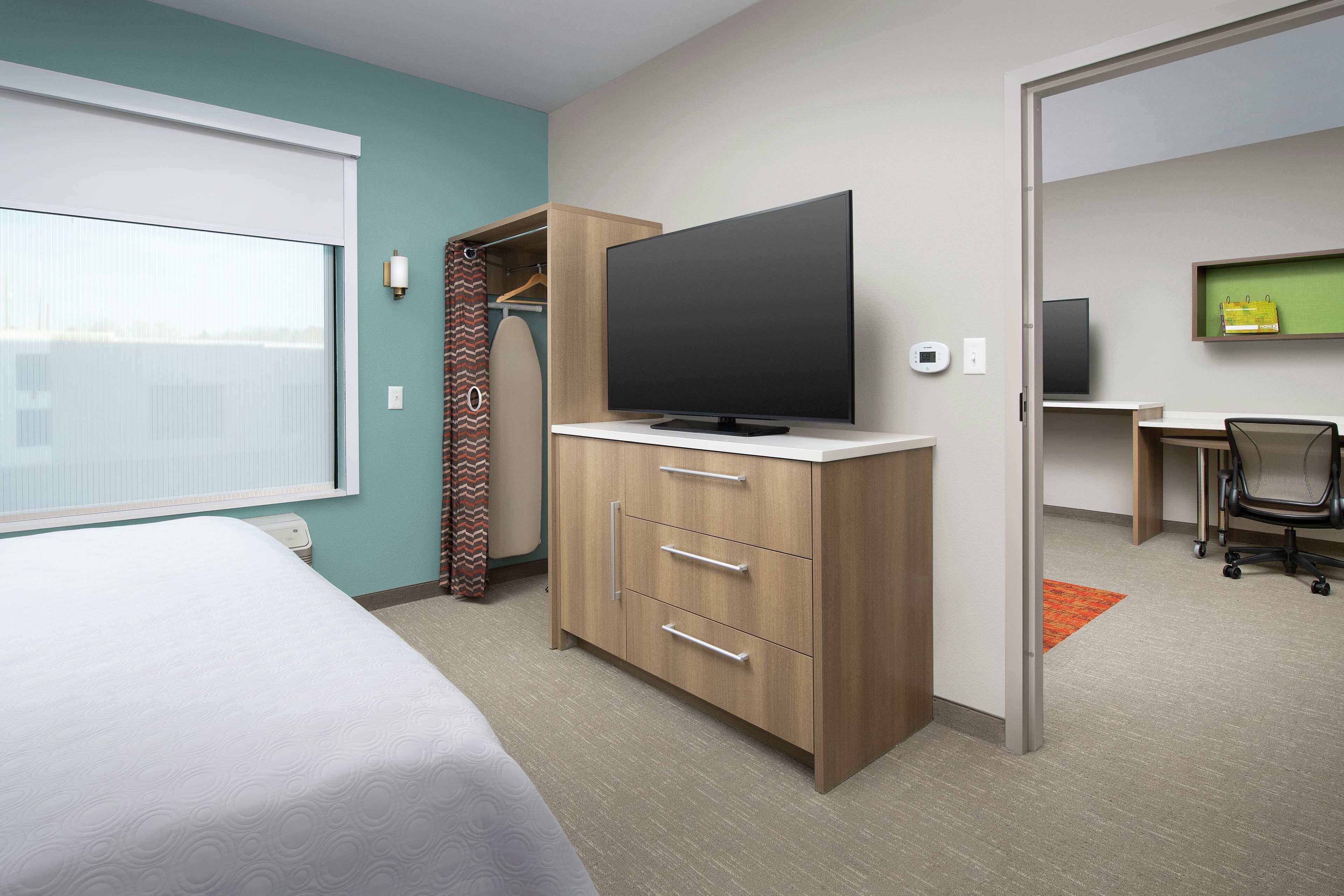 A hotel room with a bed, a TV on a wooden cabinet, a desk with a chair, and a view through a window.