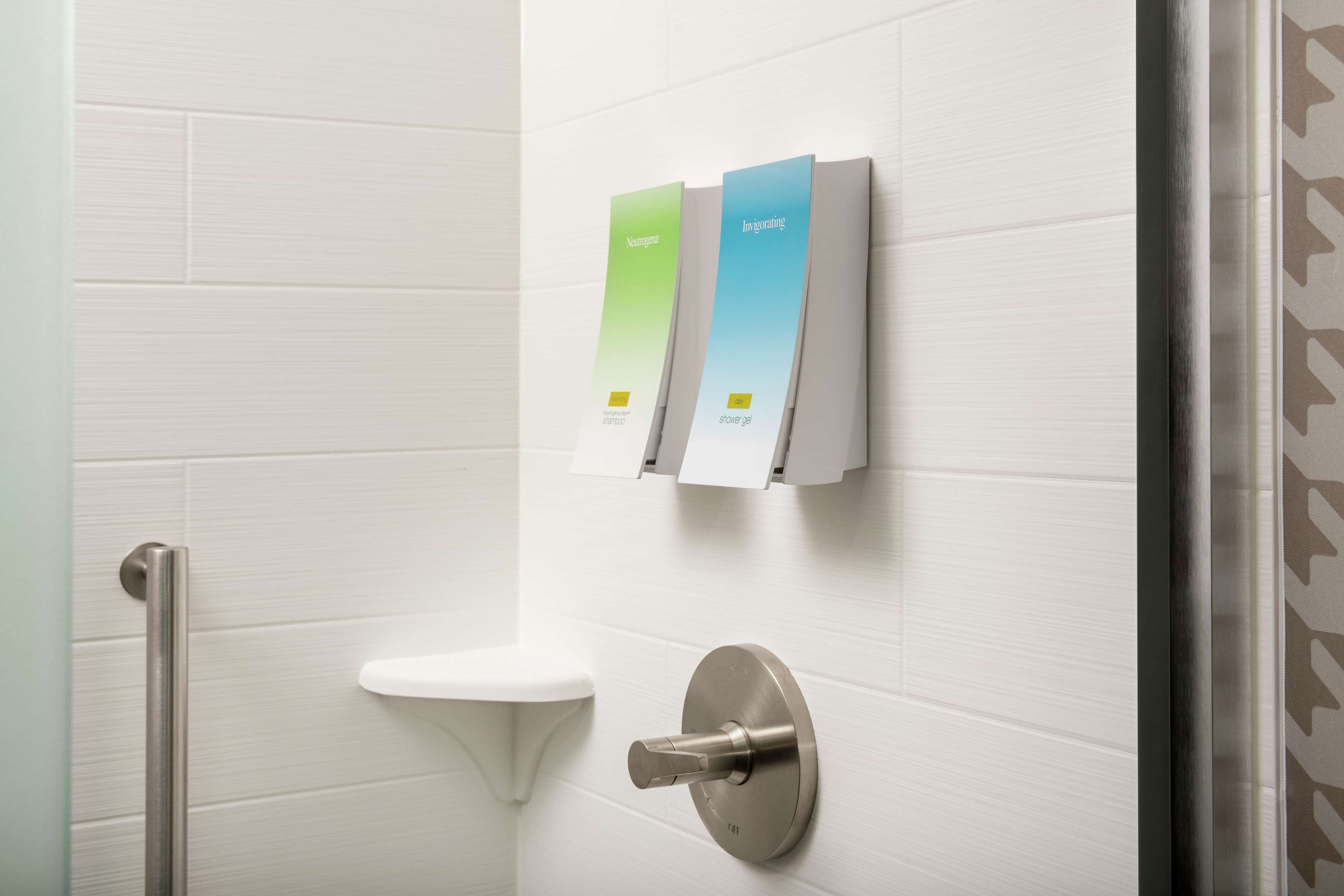 A modern bathroom with a white tiled wall, a white sink, and a shower with a control panel.