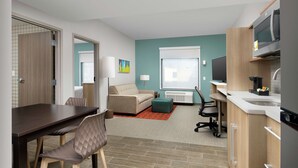 A compact hotel room with a dining area, kitchenette, and a bed.