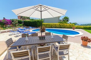 A poolside area with a table and chairs, a large umbrella, and lounge chairs.