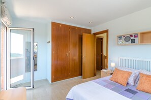 A bedroom with a bed, a nightstand, a wooden wardrobe, and a sliding glass door leading to a balcony.