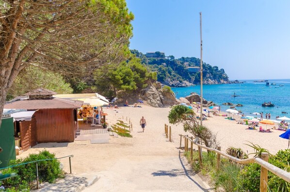 Ein Strand mit einem Holzgebäude, ein Sandweg, der zum Strand führt, und freie Sicht auf das Meer.