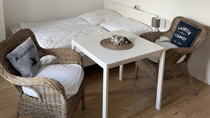 Una habitación acogedora con una cama, dos sillones de mimbre, una mesita y obras de arte en las paredes.