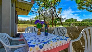 An outdoor dining area with a table set for two, surrounded by white plastic chairs, a vase with flowers, and a view of a vineyard. - Apartment Santin by Interhome (Umag/Savudrija)
