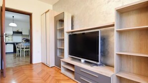 A modern living room with a flat-screen TV, wooden flooring, built-in shelving, and a kitchen visible through an open door. - Apartment Santin by Interhome (Umag/Savudrija)