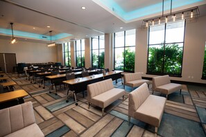 A conference room with tables, chairs, and a large window with a view of trees. - Hotel Indigo Everett - Waterfront Place by IHG (Everett)