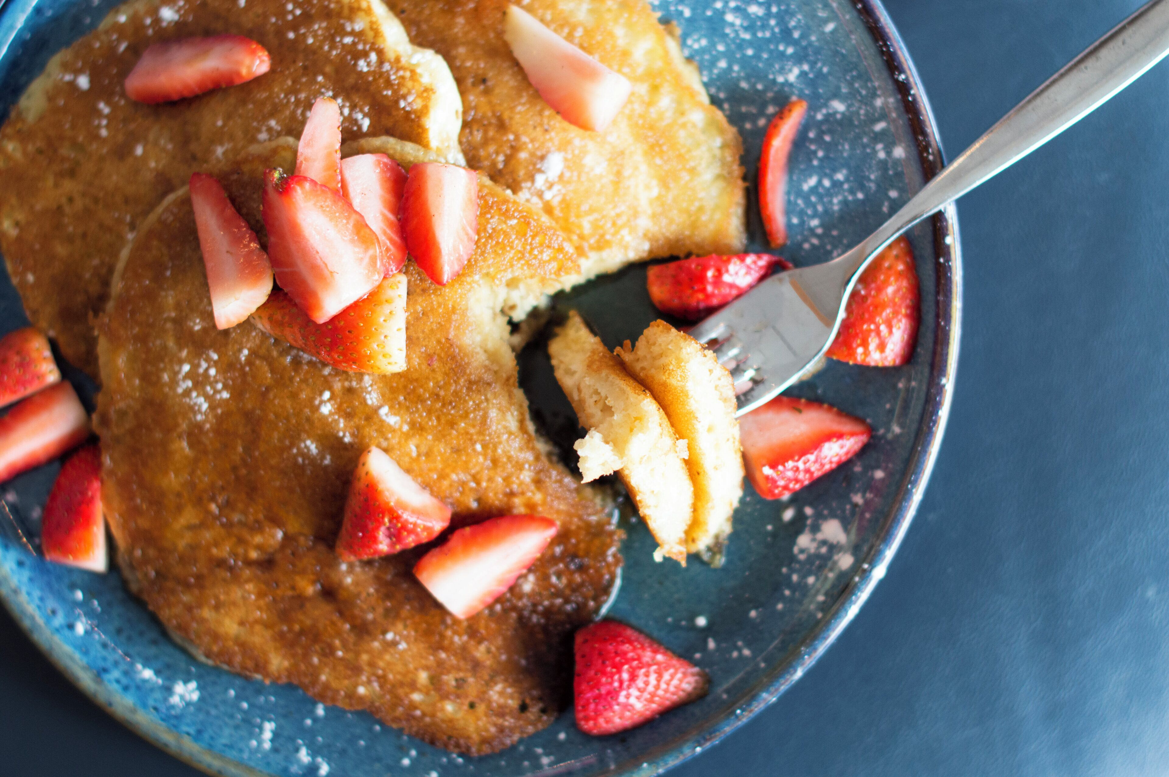 Una porción de tortitas con fresas y una cuchara.