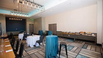 Un salón de conferencias con mesas redondas, sillas, una pantalla de proyector y una zona de bufé.