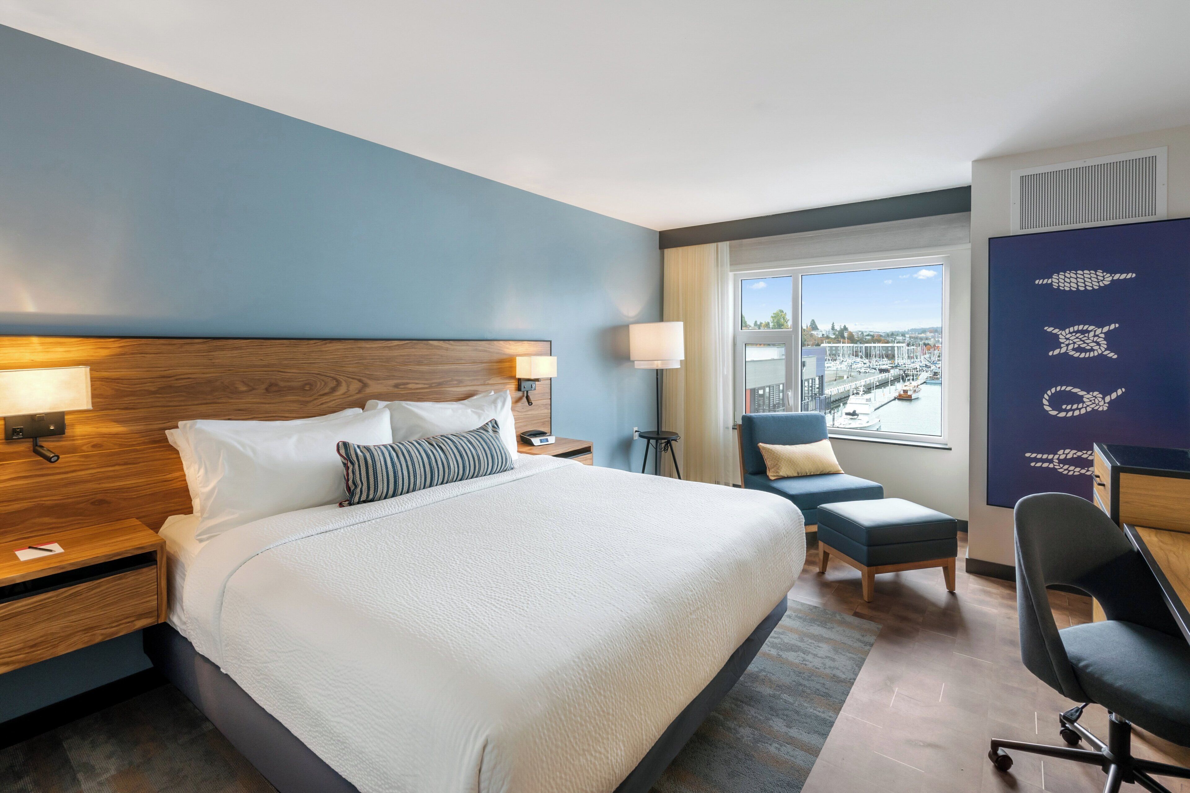 Habitación de hotel con una cama grande, un escritorio, una silla y vistas a la ciudad.