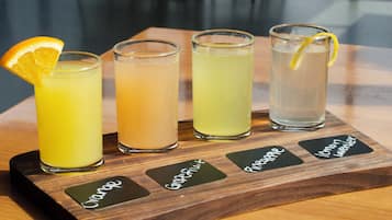 Four glasses of different beverages on a wooden tray with labels.