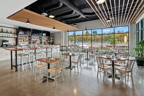A spacious indoor dining area with multiple tables and chairs, a bar area with shelves of bottles, and large windows offering a view of the outside. - Hotel Indigo Everett - Waterfront Place by IHG (Everett)