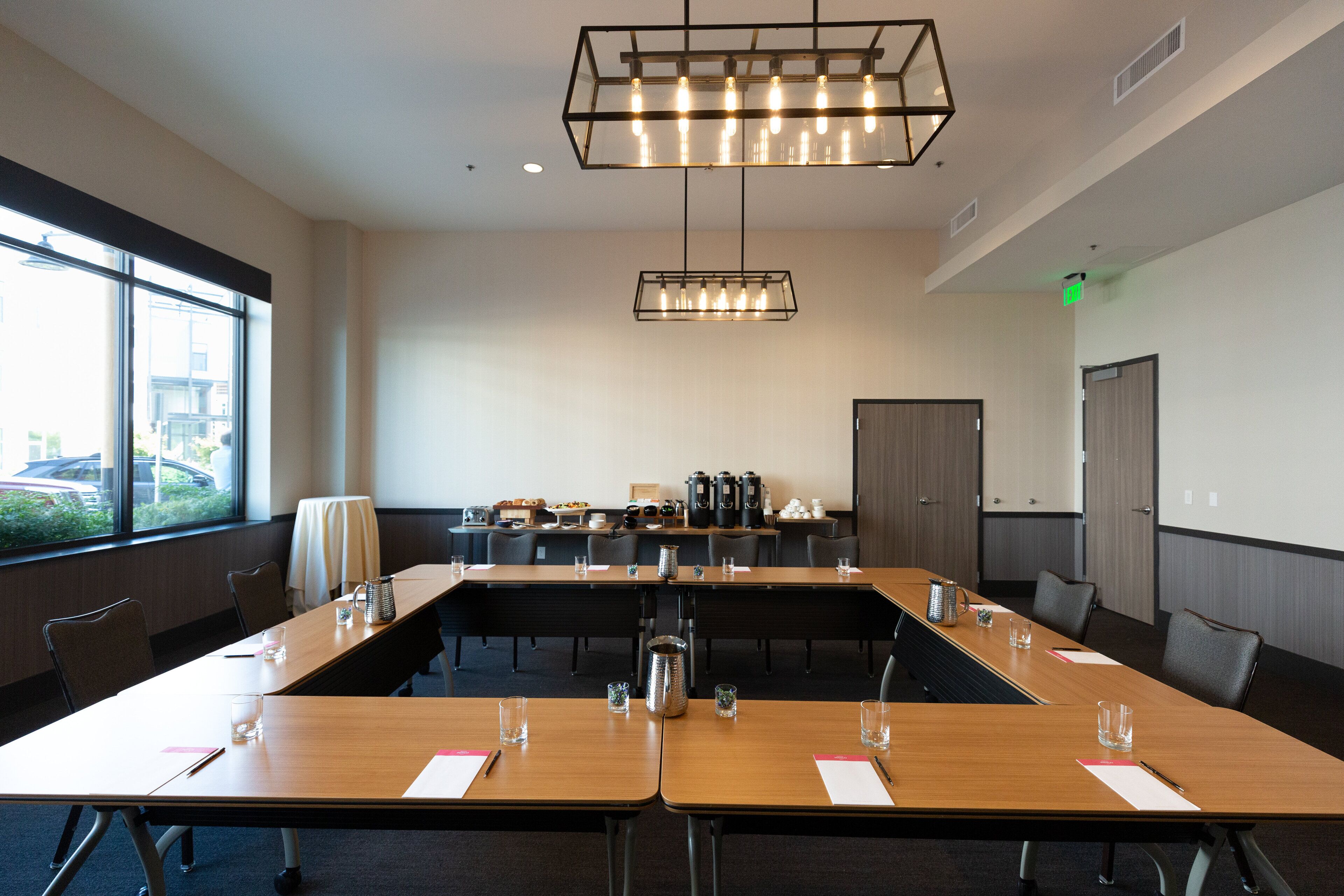 A conference room with a long table, chairs, a projector screen, and a coffee station.