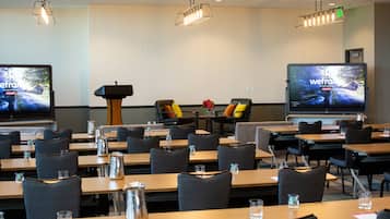 A conference room with multiple tables, chairs, and large screens displaying the same content.