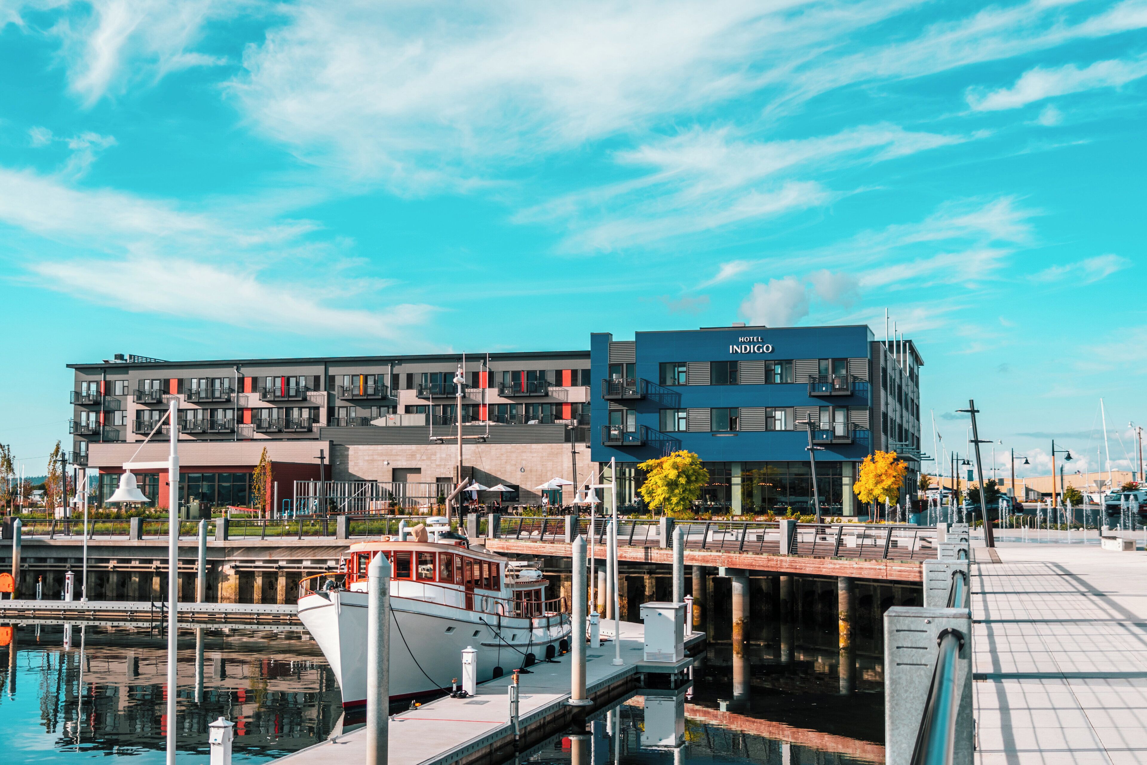 A modern hotel with a marina, featuring a dock with boats, a waterfront promenade, and a clear sky.