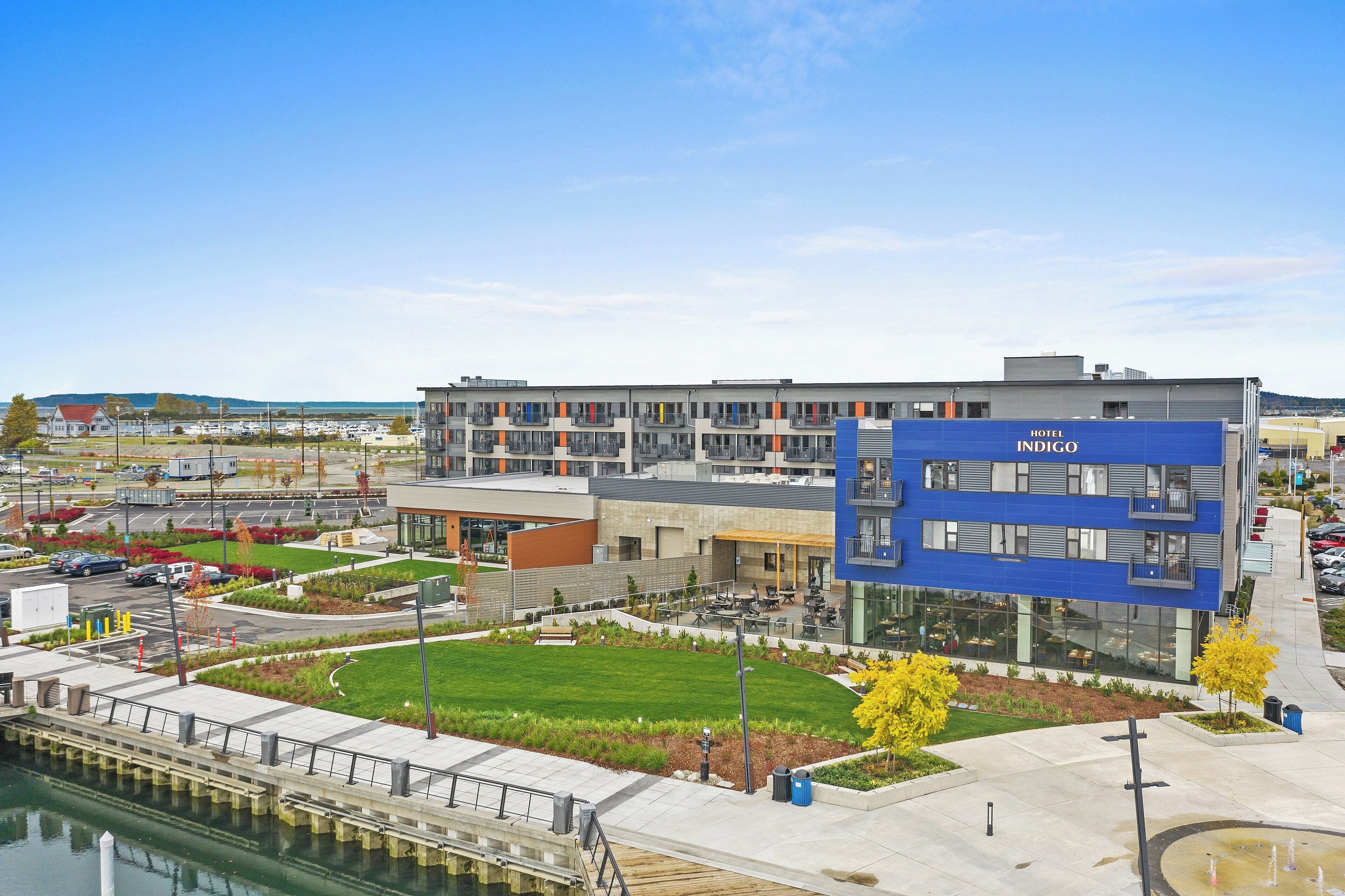 A modern hotel with a blue facade, a courtyard with outdoor seating, and a view of the water.