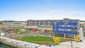 A modern hotel with a blue facade, a courtyard with outdoor seating, and a view of the water.