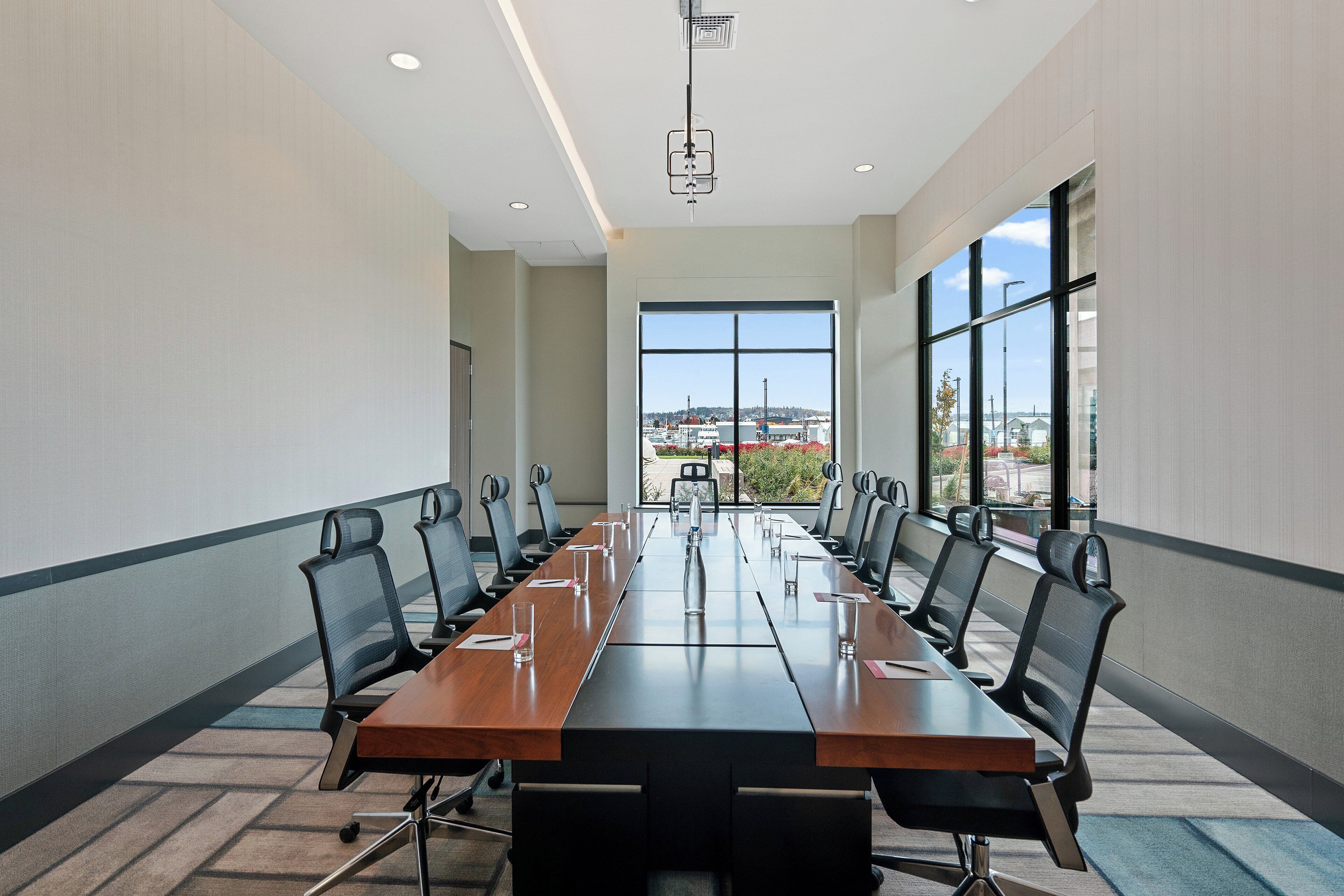 Un salón de conferencias con una larga mesa, sillas y ventanas amplias que ofrecen vistas de la ciudad.