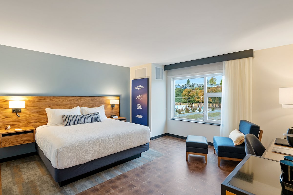 A modern hotel room with a large bed, a desk, and a view of the outdoors.