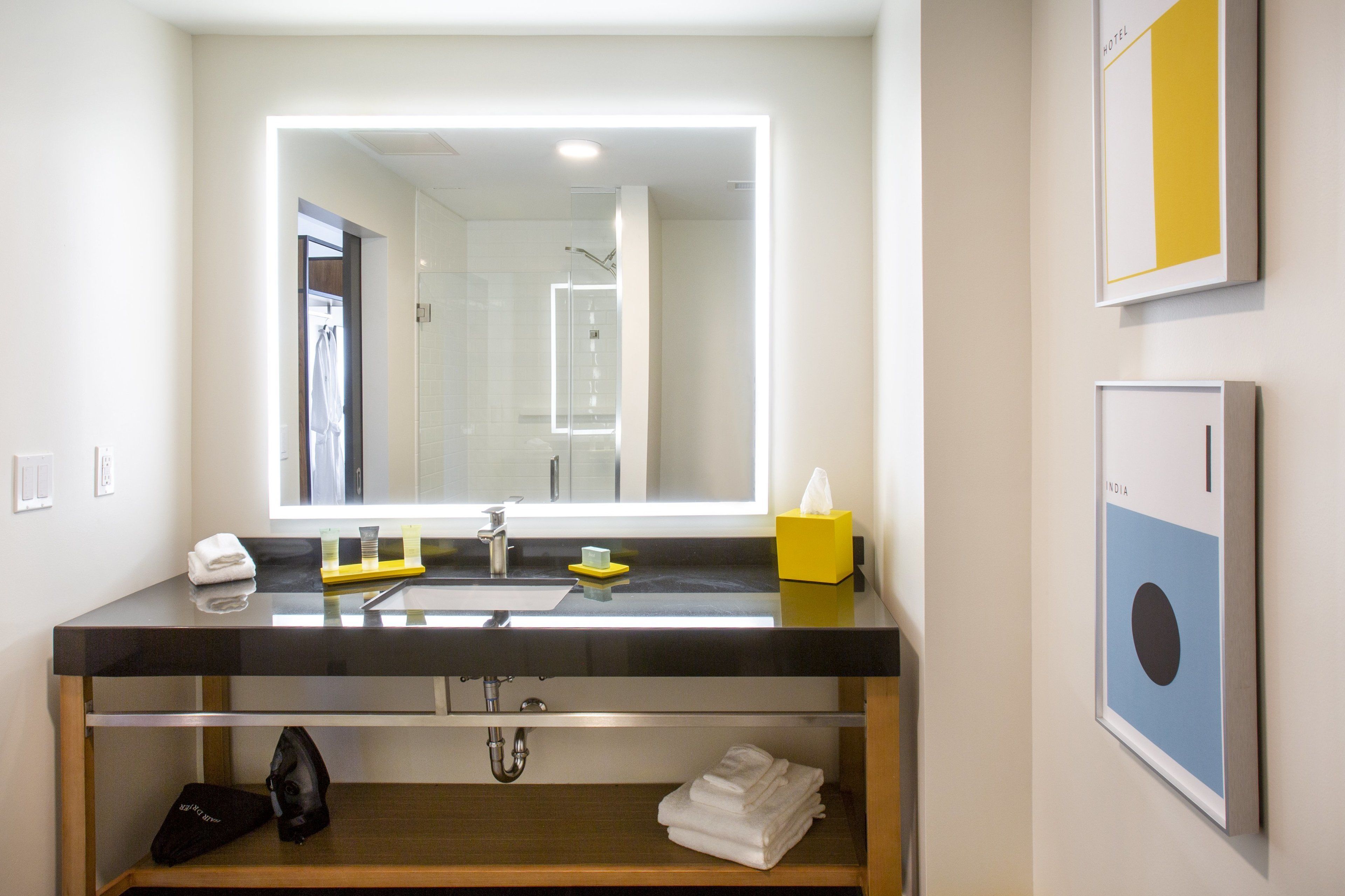 Une salle de bain moderne avec un grand miroir, un plan de toilette noir et un distributeur de savon jaune.