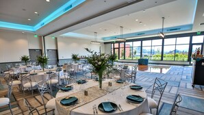 A spacious banquet hall with round tables, white chairs, and large windows offering a view of greenery. - Hotel Indigo Everett - Waterfront Place by IHG (Everett)