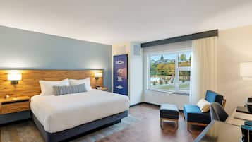 A modern hotel room with a large bed, a desk, a chair, and a view of the outdoors.