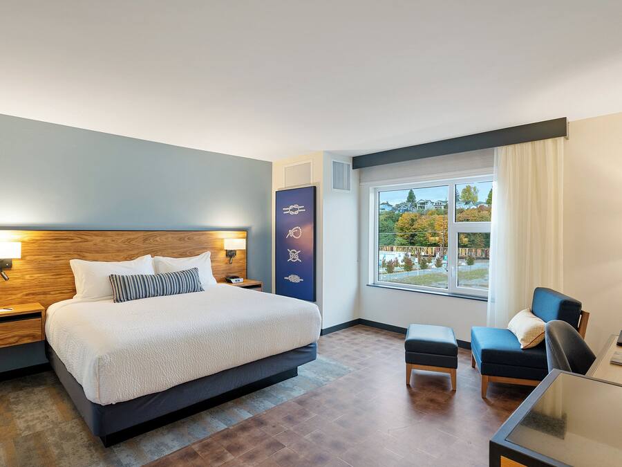 A modern hotel room with a large bed, a desk, a chair, and a view of the outdoors.